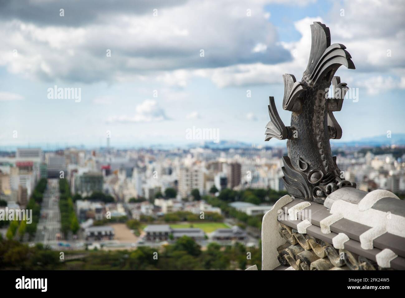 Koi carp Tiger headed fish statue on roof top of Himeji Castle with view of Himeji City (soft focus), Japan Stock Photo