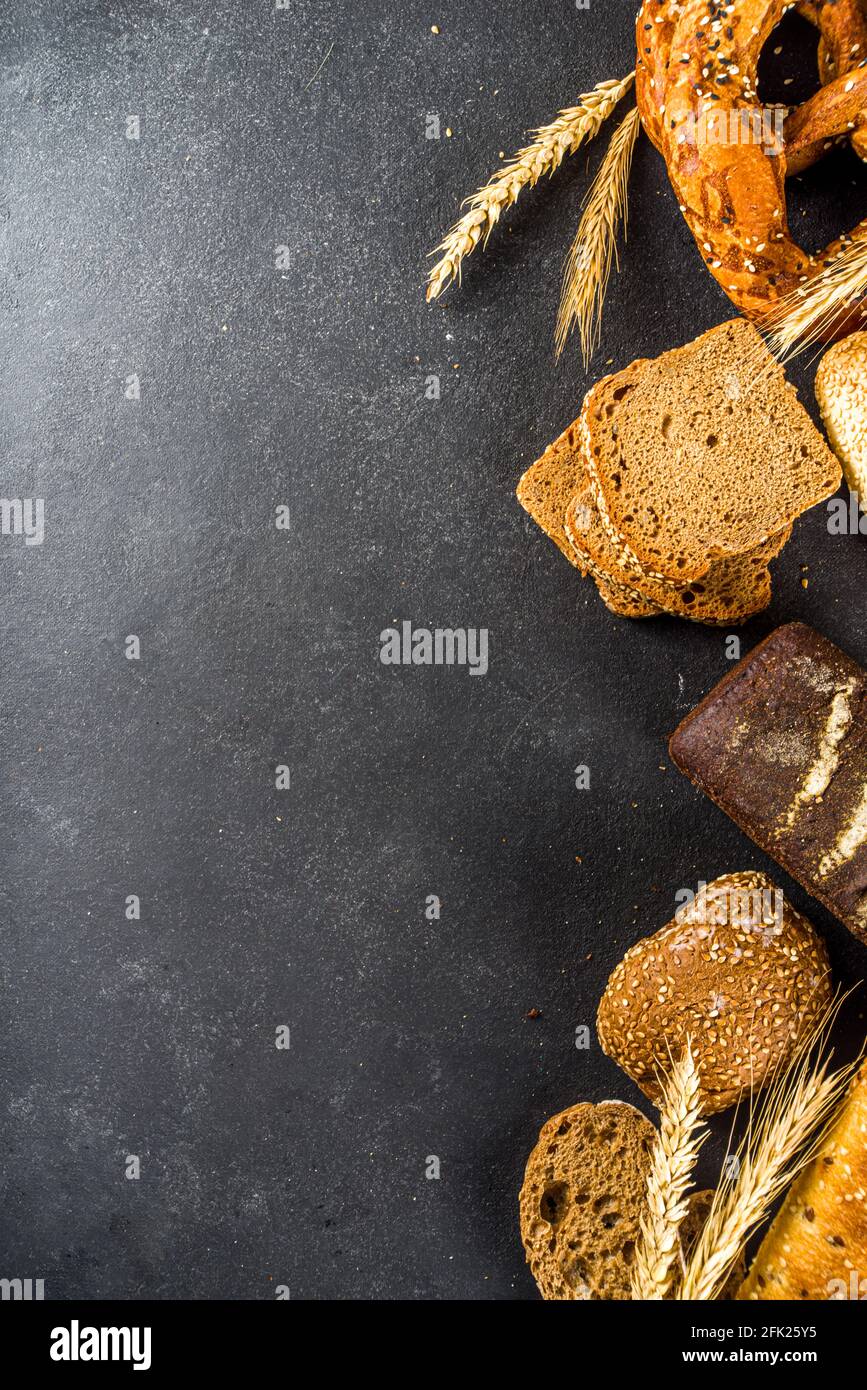 Assortment of various delicious freshly baked bread, on black concrete background top view copy space Stock Photo
