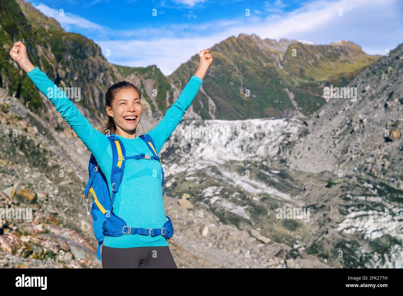 Excited cheering woman on travel adventure excited to travel again. Tourist explorer backpacking nature landscape by Franz Josef Glacier, Westland Tai Stock Photo