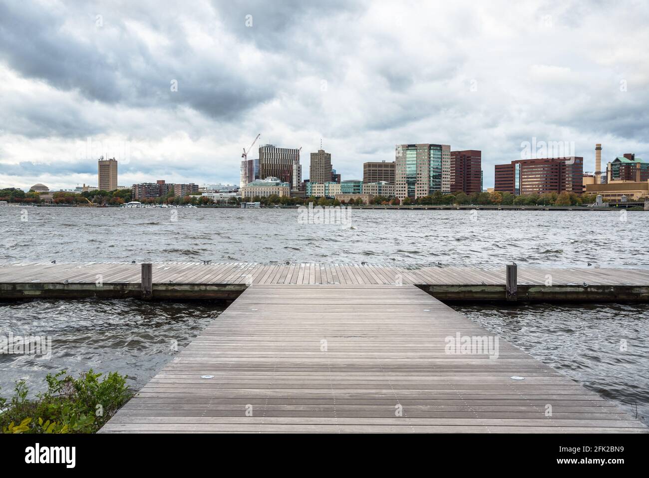 Deserted pier on a wide river with an urban skyline in background on a stormy autumn day Stock Photo