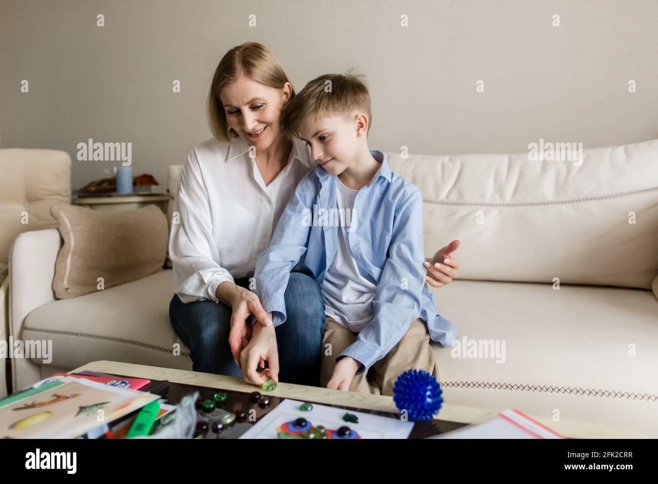 Adult woman and a teenager are sitting behind on the couch playing a board game. Stock Photo