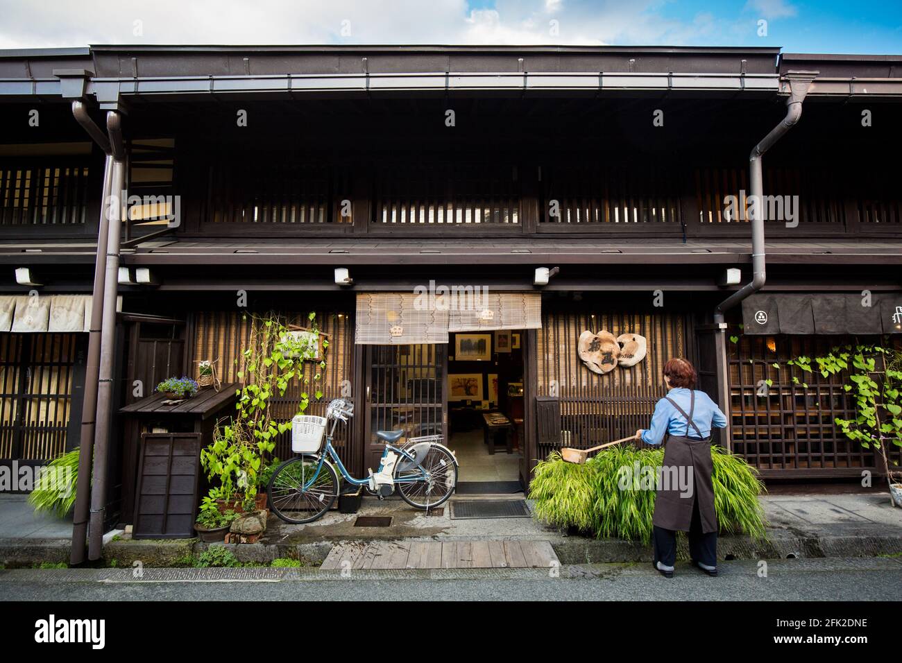 Japanese woman watering green plants outside traditional Japanese