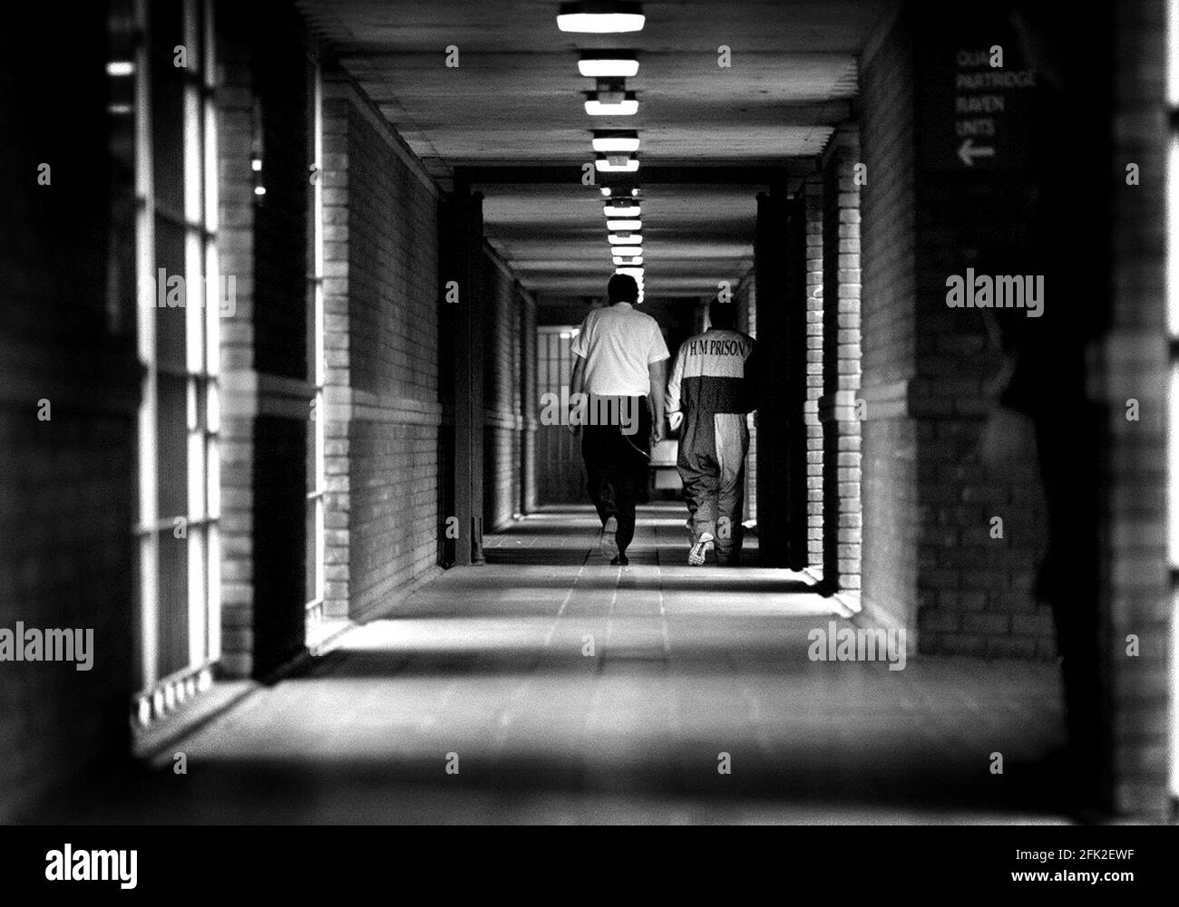 Prisoners at  Remand Centre Feltham March 1999A prison officer and a prisoner walking along a corridor in one of the house blocks The prisoner is wearing a special unifrom to identify him as an escape risk at HM Young Offenders Institution and Remand Centre Feltham   Richard Tilt the Director General of the Prison Service visitied the institution today the day before his retirement Stock Photo