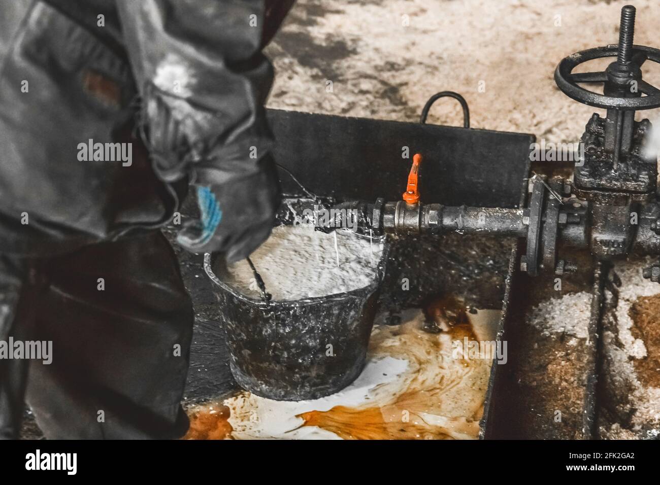 Draining the condensate mixture oil in a bucket from the air compressor pipe at an industrial plant. Stock Photo