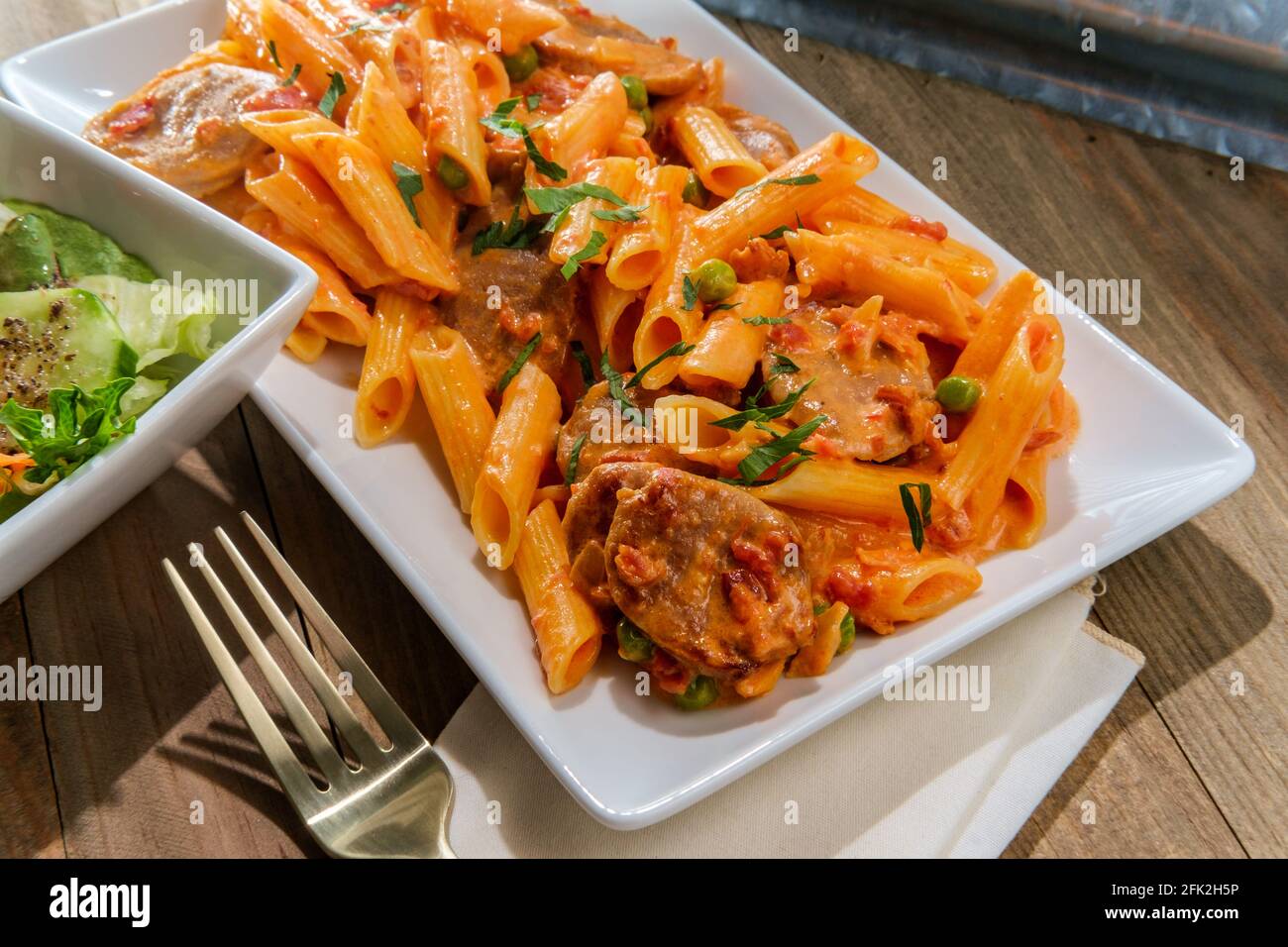Italian penne alla vodka pink cream sauce with sliced spicy sausage and side salad Stock Photo