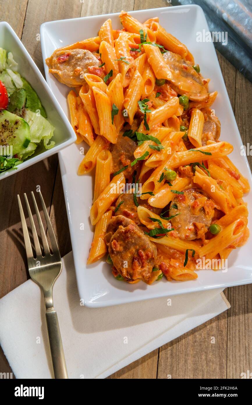 Italian penne alla vodka pink cream sauce with sliced spicy sausage and side salad Stock Photo