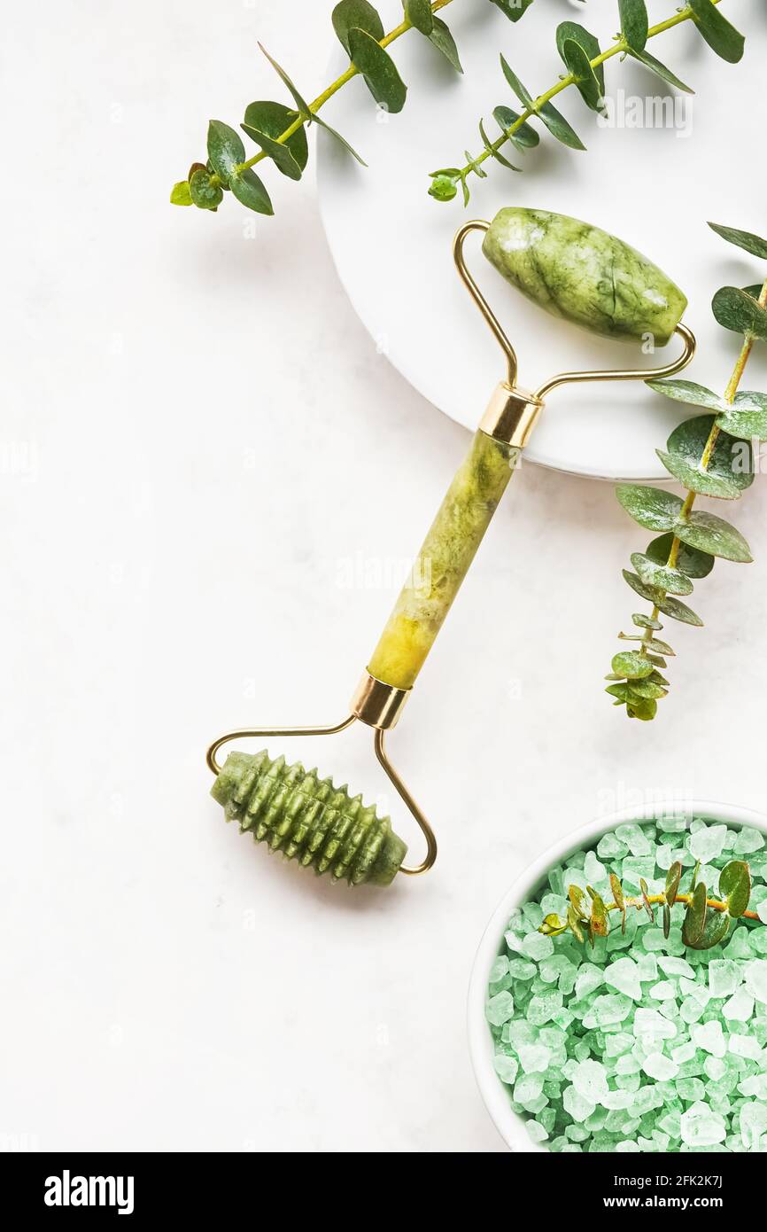 Green face roller from natural jade stone and eucalyptus branches on a white background. SPA concept. Top view, copy space for text Stock Photo