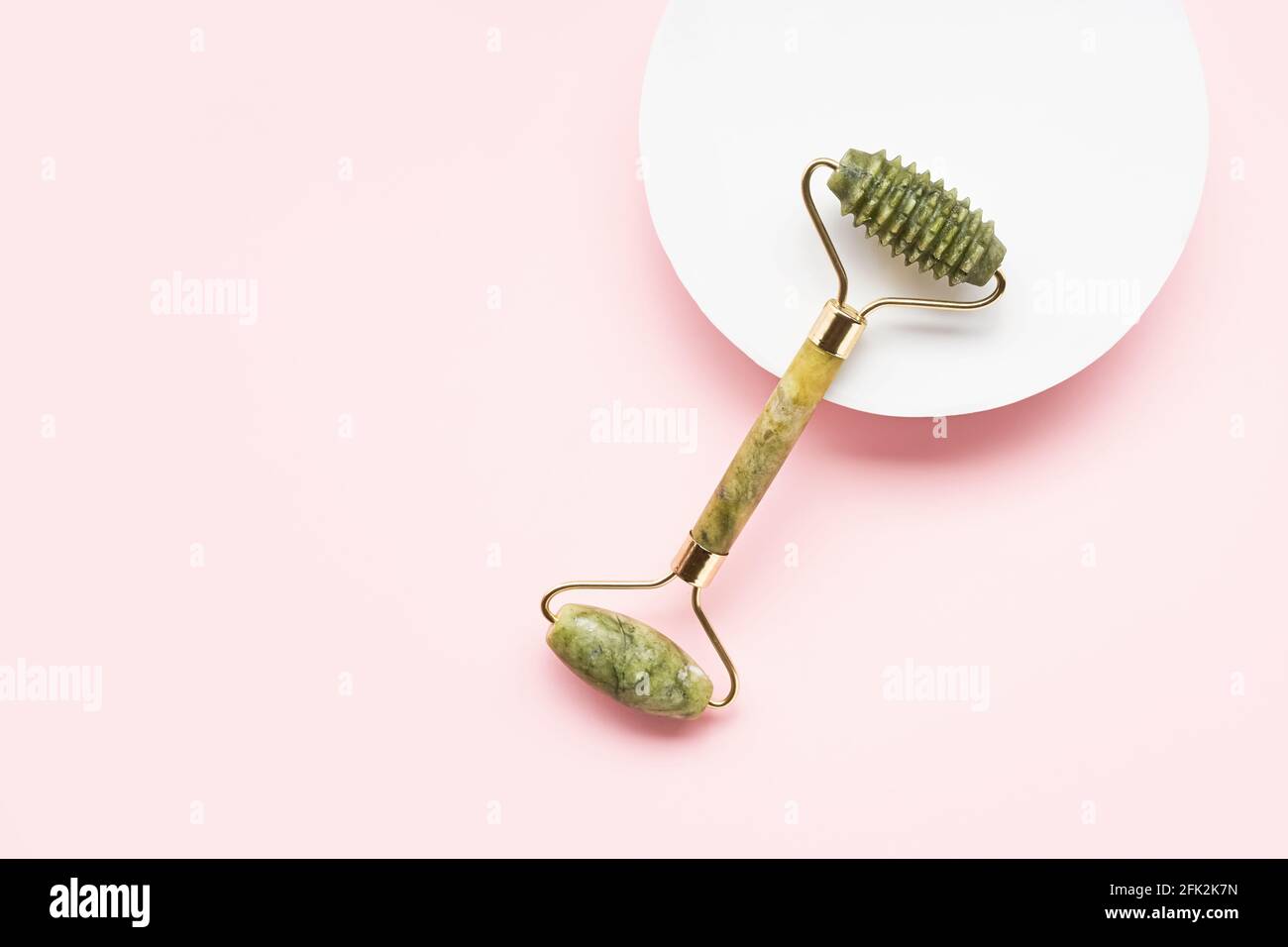 Green face roller from natural jade stone on a pink background. SPA concept. Top view, copy space for text Stock Photo