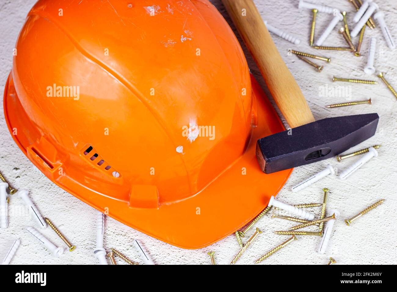 Orange protective hard hat with claw hammer on light gray cement. Home repairing and improvement, house building concept. Stock Photo