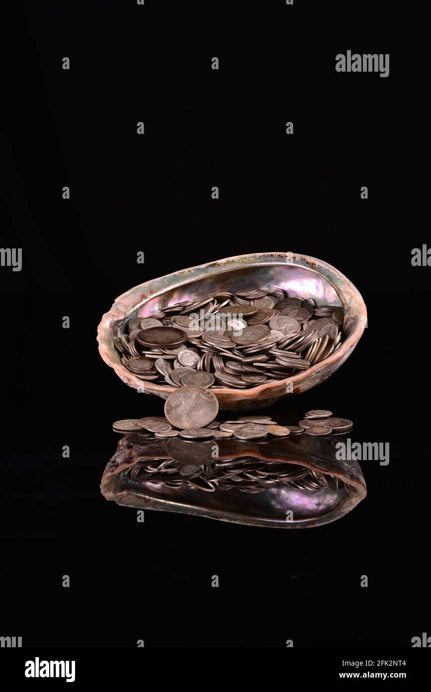 A colorful large abalone shell overflowing with real silver USA coins. The beautiful treasure seashell is full or obsolete silver coins. Stock Photo