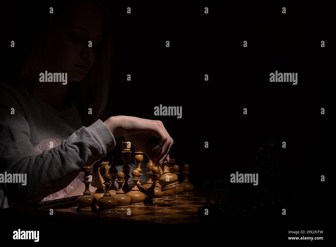 girl in the shadows plays vintage chess on a dark background. old chess. business concept. Stock Photo