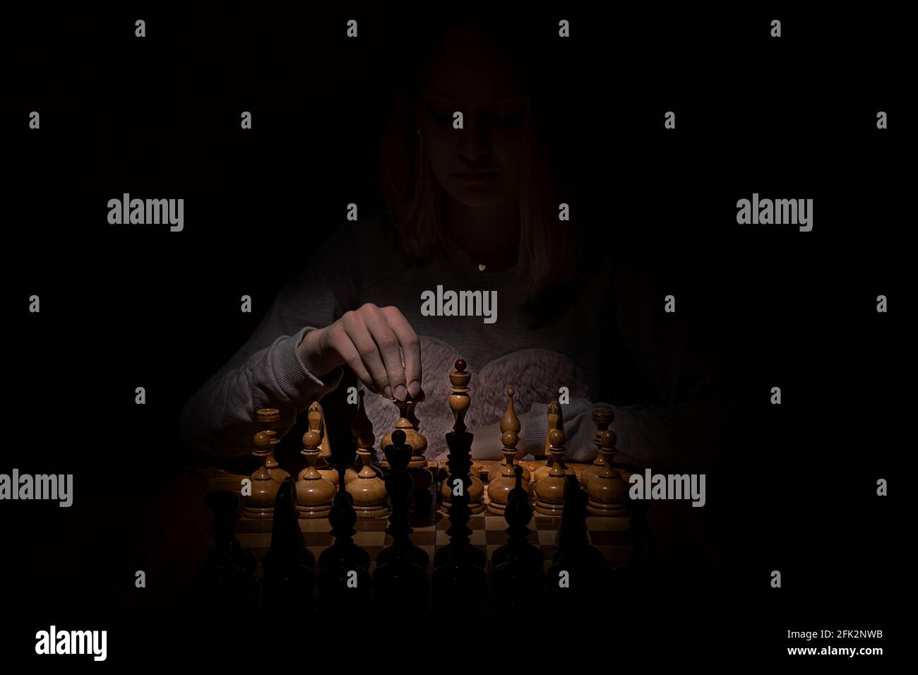 girl in the shadows plays vintage chess on a dark background. old chess. business concept. Stock Photo