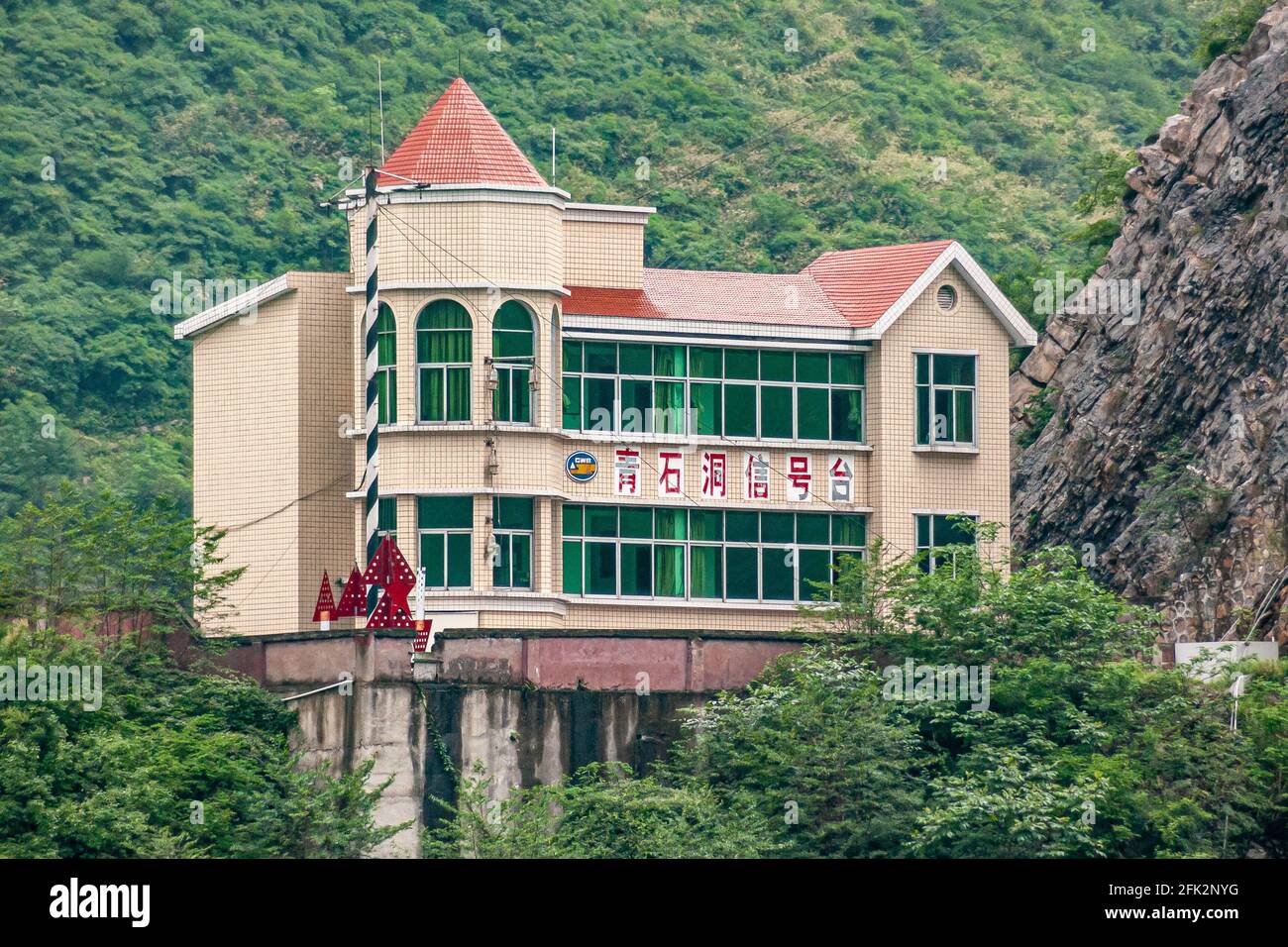 Guandukou, Hubei, China - May 7, 2010: Wu Gorge on Yangtze River. Red roofed modern yellow stone buildings on platform rises above green foliage again Stock Photo