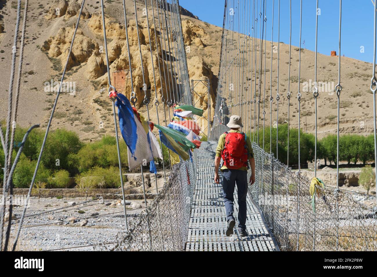 Trekker crossing a bridge adorned with Tibetan prayer flags  in Chuksang, Upper Mustang region, Nepal. Stock Photo