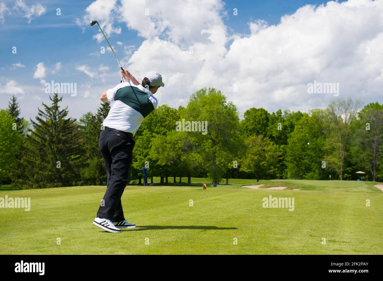 A golfer watches his ball flying towards the green. Stock Photo