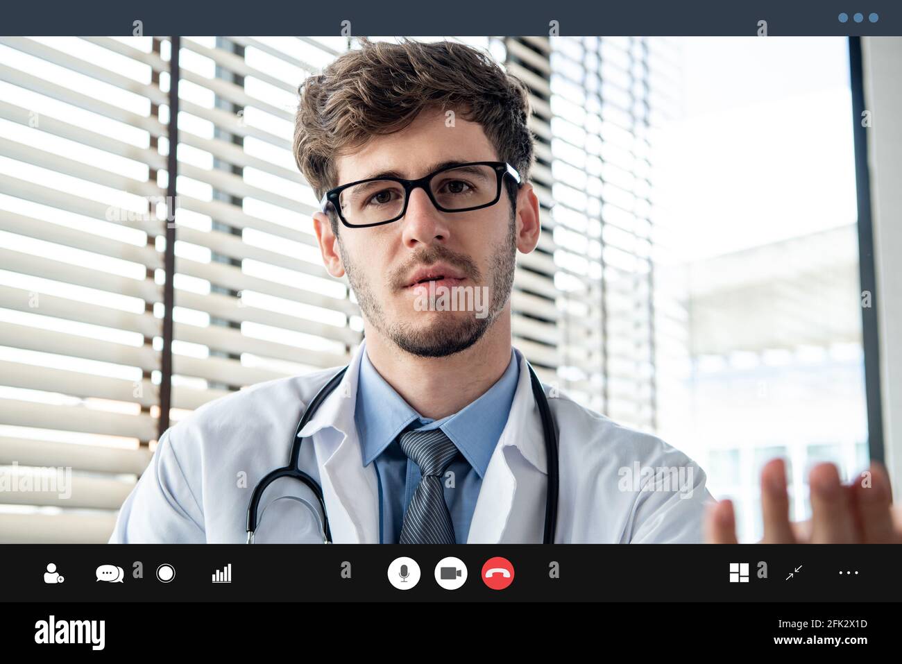 Young male doctor seriously explaining somthing to patient via online video calling application, telehealth concepts Stock Photo