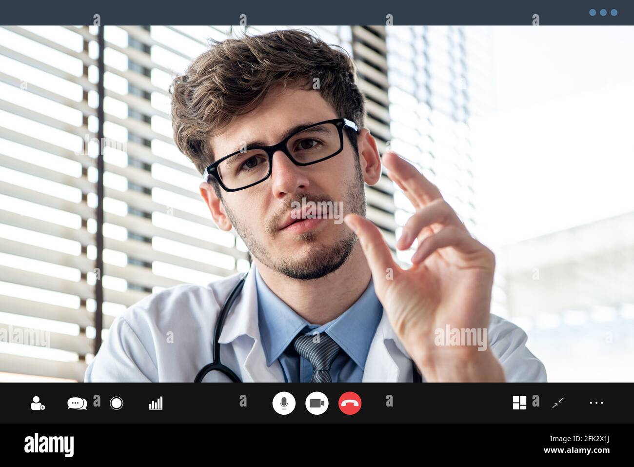 Young male doctor seriously explaining somthing to patient via online video calling application, telehealth concepts Stock Photo