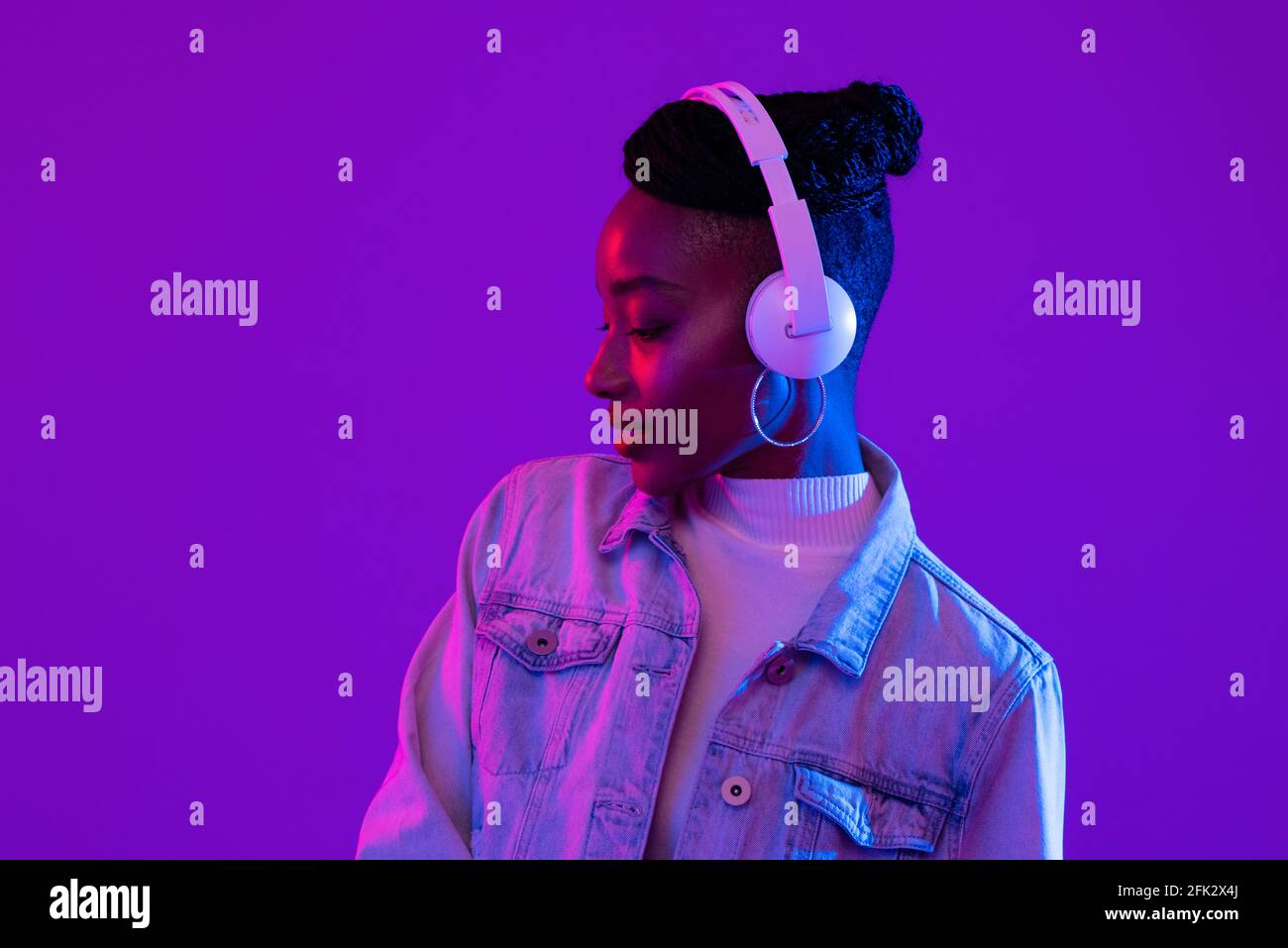 Young African American woman wearing headphones listening to music in futuristic purple cyberpunk neon light background Stock Photo