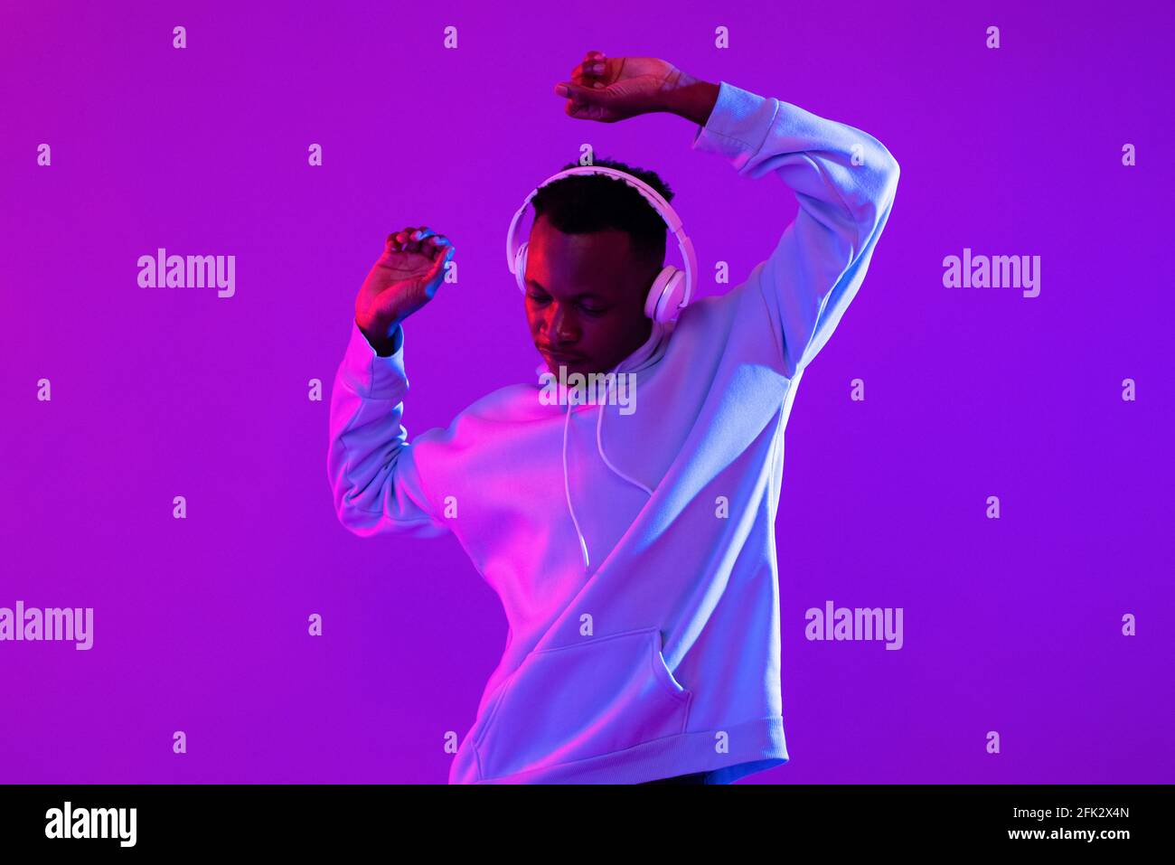 Young handsome African man wearing headphones listening to music and dancing in futuristic purple cyberpunk neon light background Stock Photo