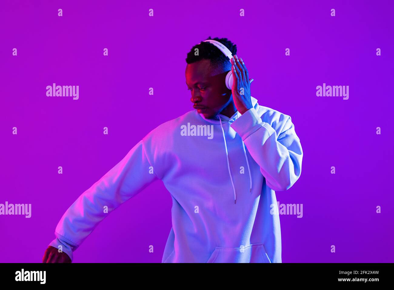 Young handsome African man wearing headphones listening to music and dancing in futuristic purple cyberpunk neon light background Stock Photo