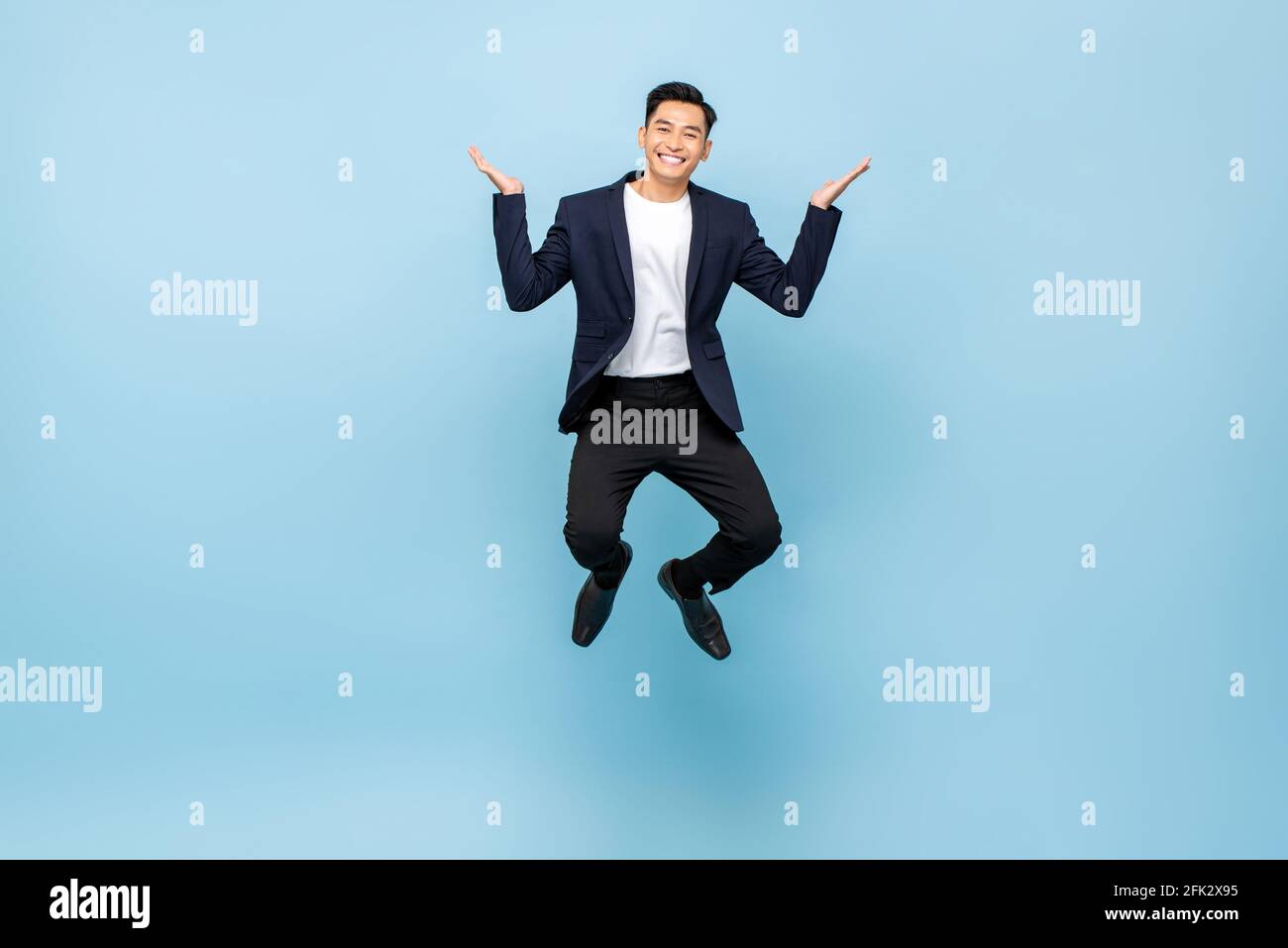Full lenght portrait of happy Asian man jumping and smiling with open hands on isolated light blue studio background Stock Photo