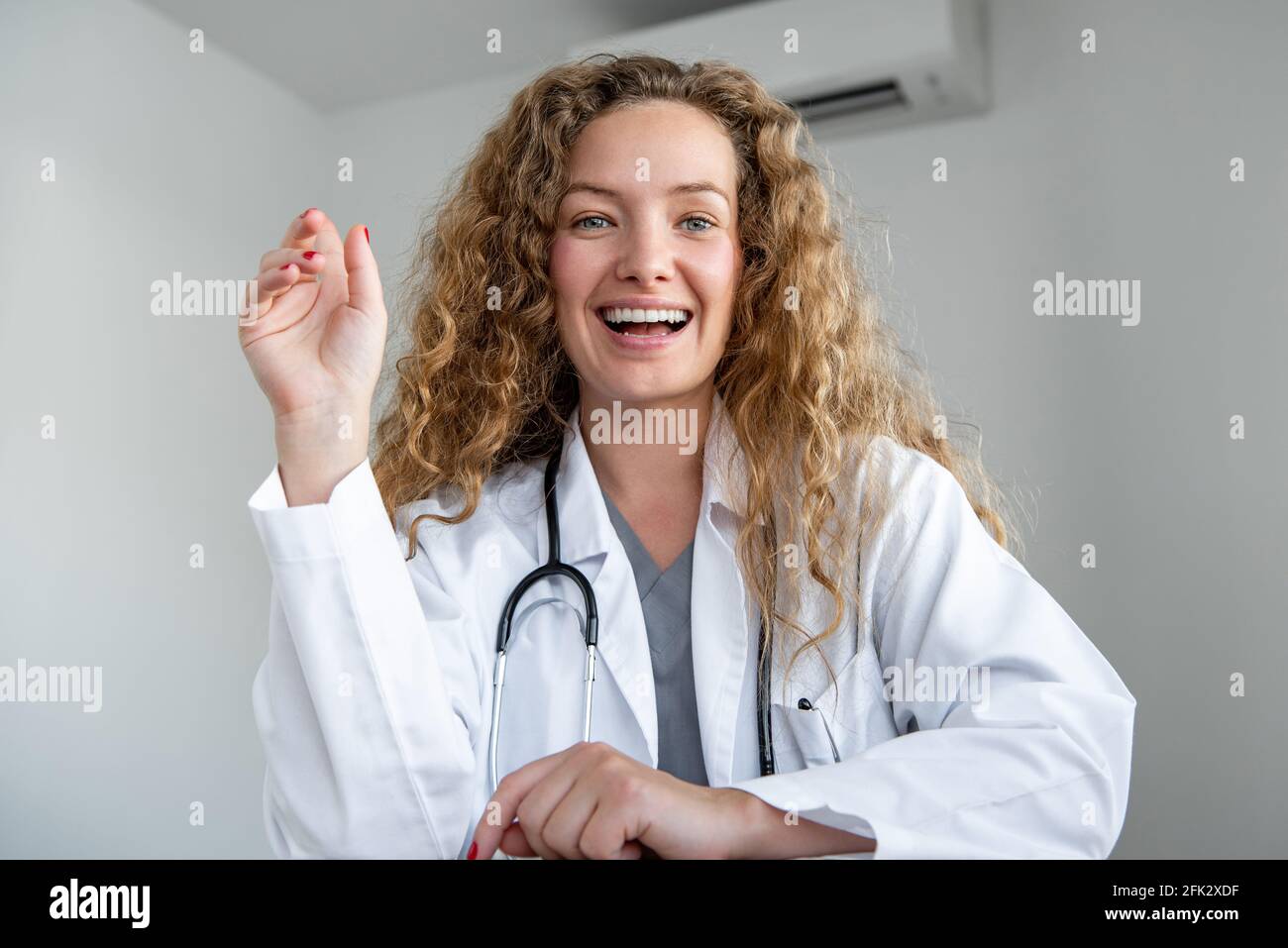 Cheerful smiling young female doctor looking at camera greeting patient online via video calling, home medical consulation service concepts Stock Photo