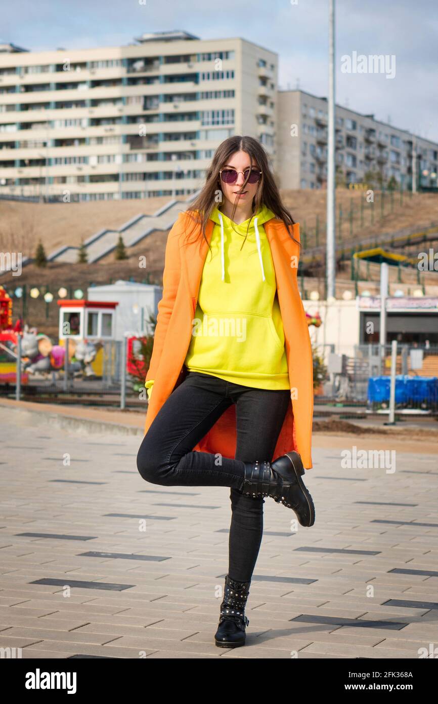 Full-length portrait good-looking young woman in vivid outfit. Trendy  female model in sunglasses, orange coat, yellow hoodie and black jeans.  Millennial hipster girl walks around the city Stock Photo - Alamy