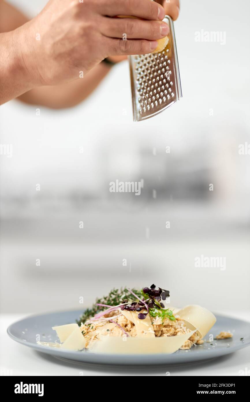 Close up of chef grate cheese for porridge with parmesan and herbs in beautiful blue plate. Concept of process cooking tasty and healthy dish with good ingredients for weight body.  Stock Photo