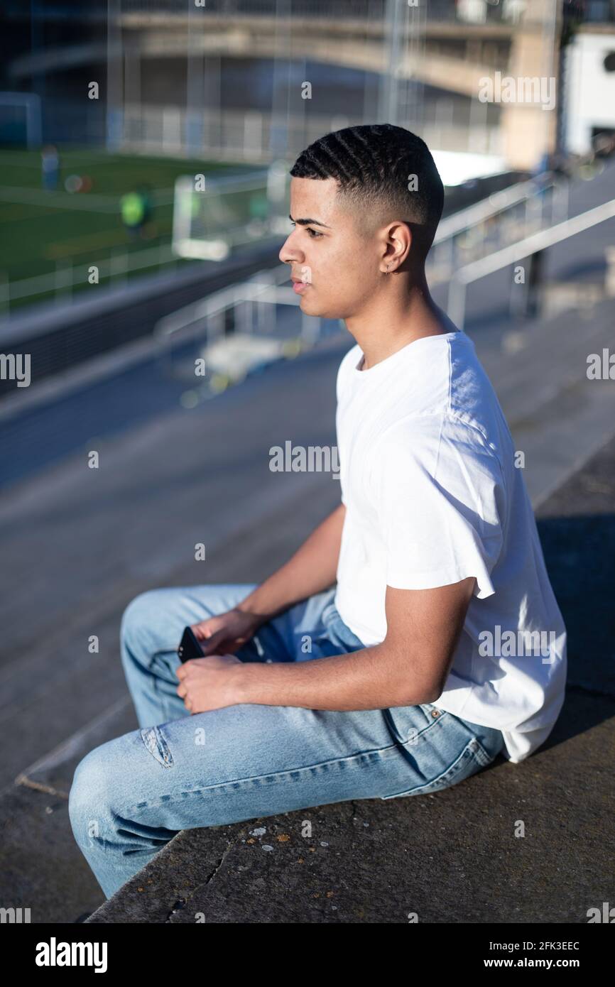 A young handsome man in t-shirt and jeans sits on a stadium bleachers alone  Stock Photo - Alamy