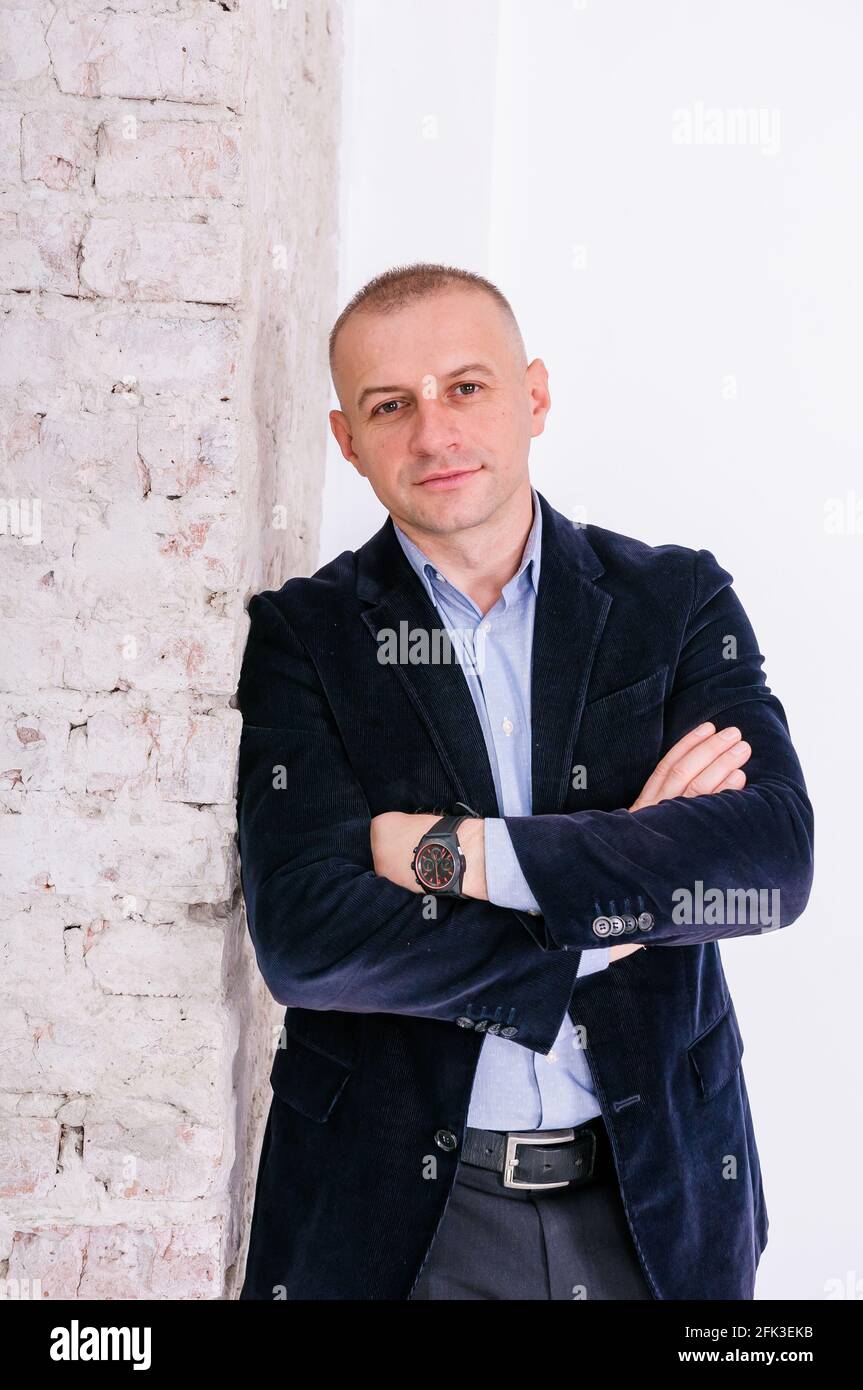 Man in blue shirt, black trousers and blue jacket on brick wall background Stock Photo