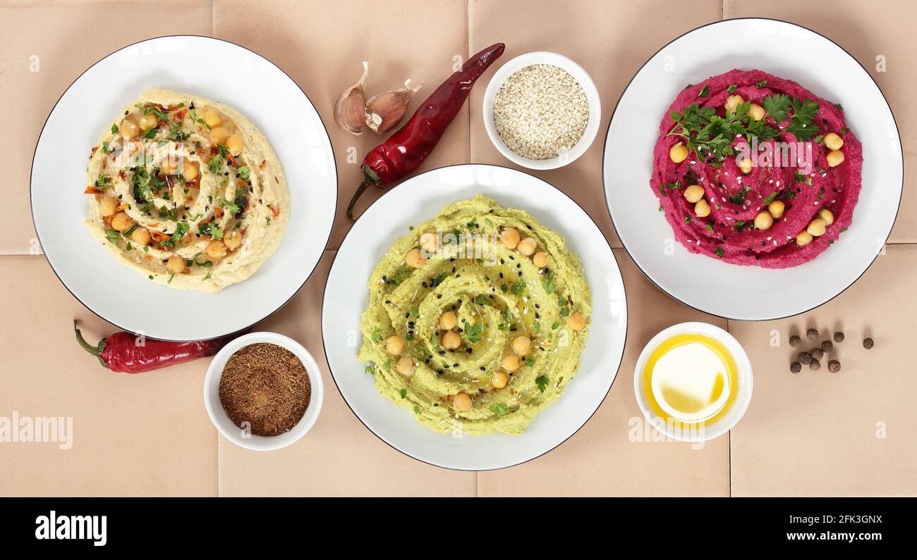 Variety of colored hummus: red, green, yellow - vegan lebanese meal, from above overhead top view, banner or background texture, vegan and vegetarian Stock Photo