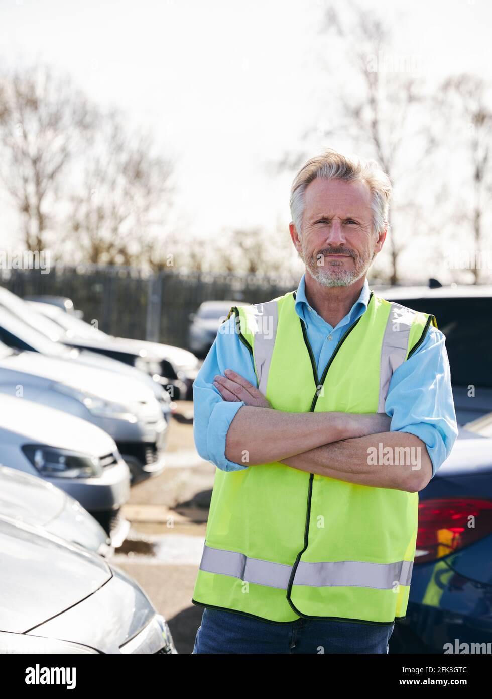 Portrait of mature male car park attendant wearing hivis safety vest folding arms Stock Photo