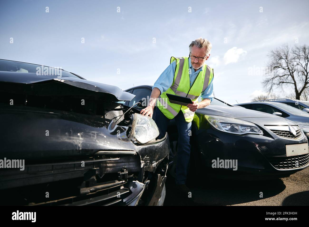 Mature male loss adjuster wearing hi-vis safety vest standing in compound  for damaged cars compiling insurance claim report on digital tablet Stock  Photo - Alamy