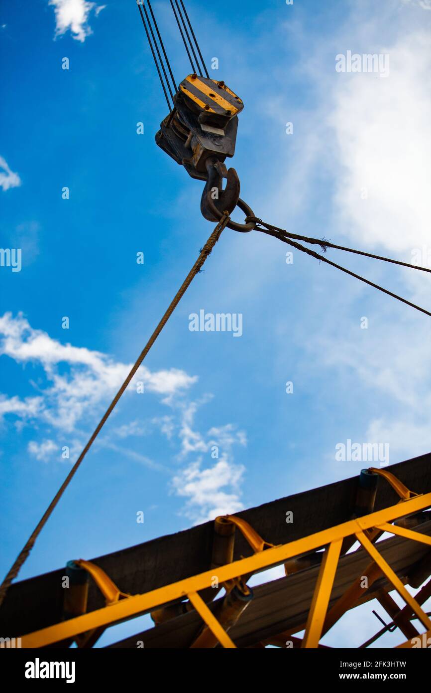 Yellow crane hook with steel wire rope lifting yellow steel girder. on blue sky with clouds background. Sunny day. Stock Photo