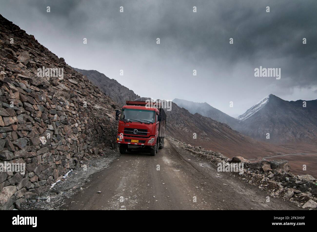 Heavy freight trucks and articulated lorries navigate along the unpaved G216 highway connecting Urumuqi to the Bayingolin Prefecture across the snow-covered Tianshan mountains in Xinjiang, China, PRC. © Time-Snaps Stock Photo