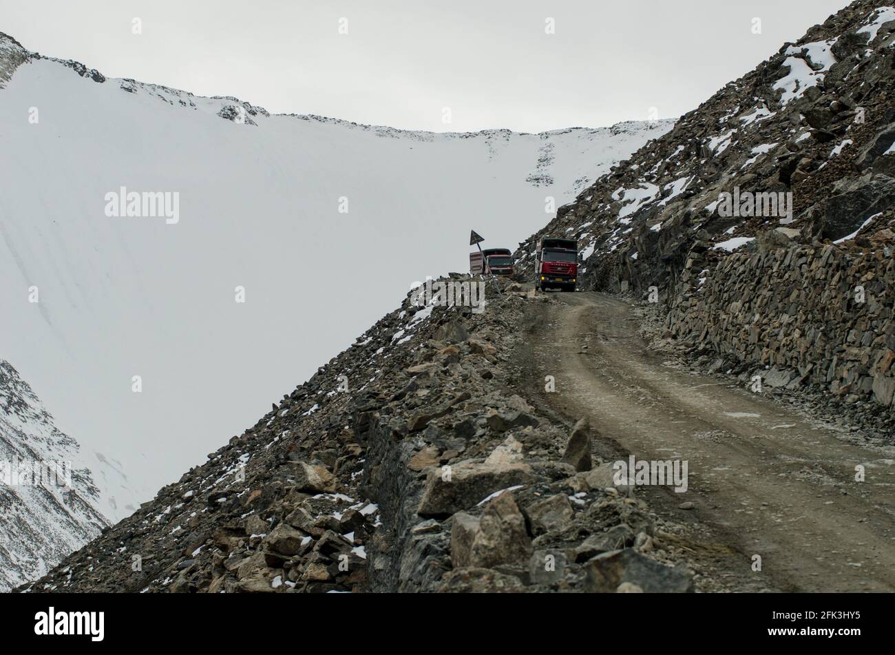 Heavy freight trucks and articulated lorries navigate along the unpaved G216 highway connecting Urumuqi to the Bayingolin Prefecture across the snow-covered Tianshan mountains in Xinjiang, China, PRC. © Time-Snaps Stock Photo