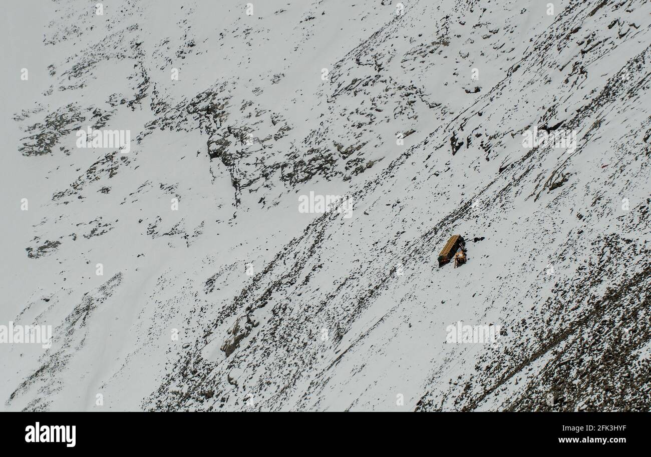 The wreck of a heavy freight trucks lies on the slopes of below the unpaved G216 highway connecting Urumuqi to the Bayingolin Prefecture across the snow-covered Tianshan mountains in Xinjiang, China, PRC. © Time-Snaps Stock Photo