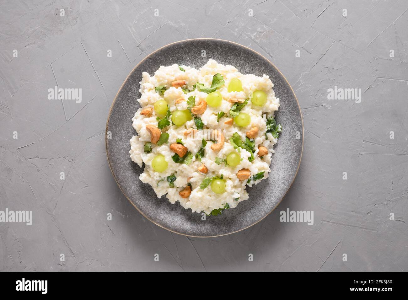 Curd Rice with cashews, grapes, cilantro on a grey background. Top view. Indian South cuisine Stock Photo