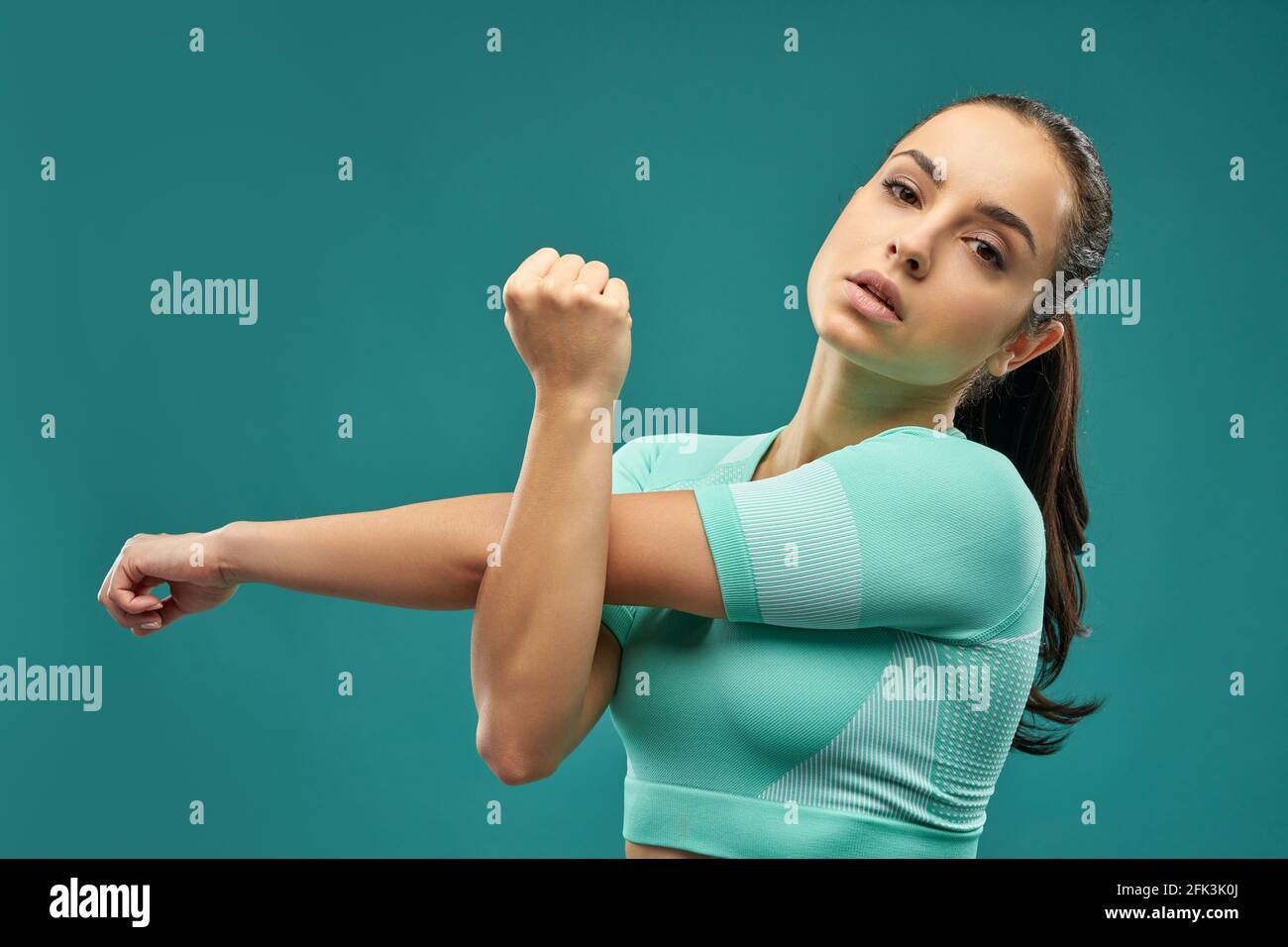 Sporty young woman stretching hands against green background Stock Photo
