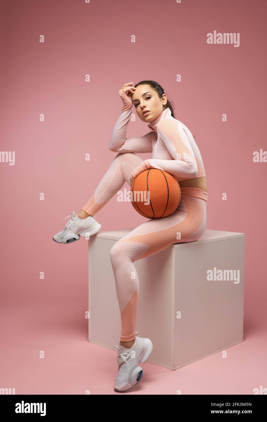 Beautiful young woman with basketball ball sitting on cube Stock Photo -  Alamy
