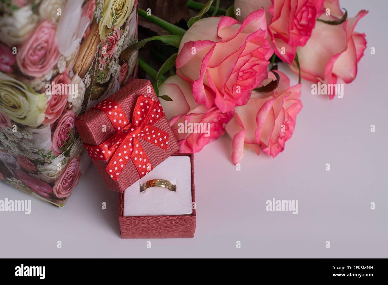 Gold wedding ring in a red box and a bouquet of pink roses. Romance. Marriage proposal Stock Photo