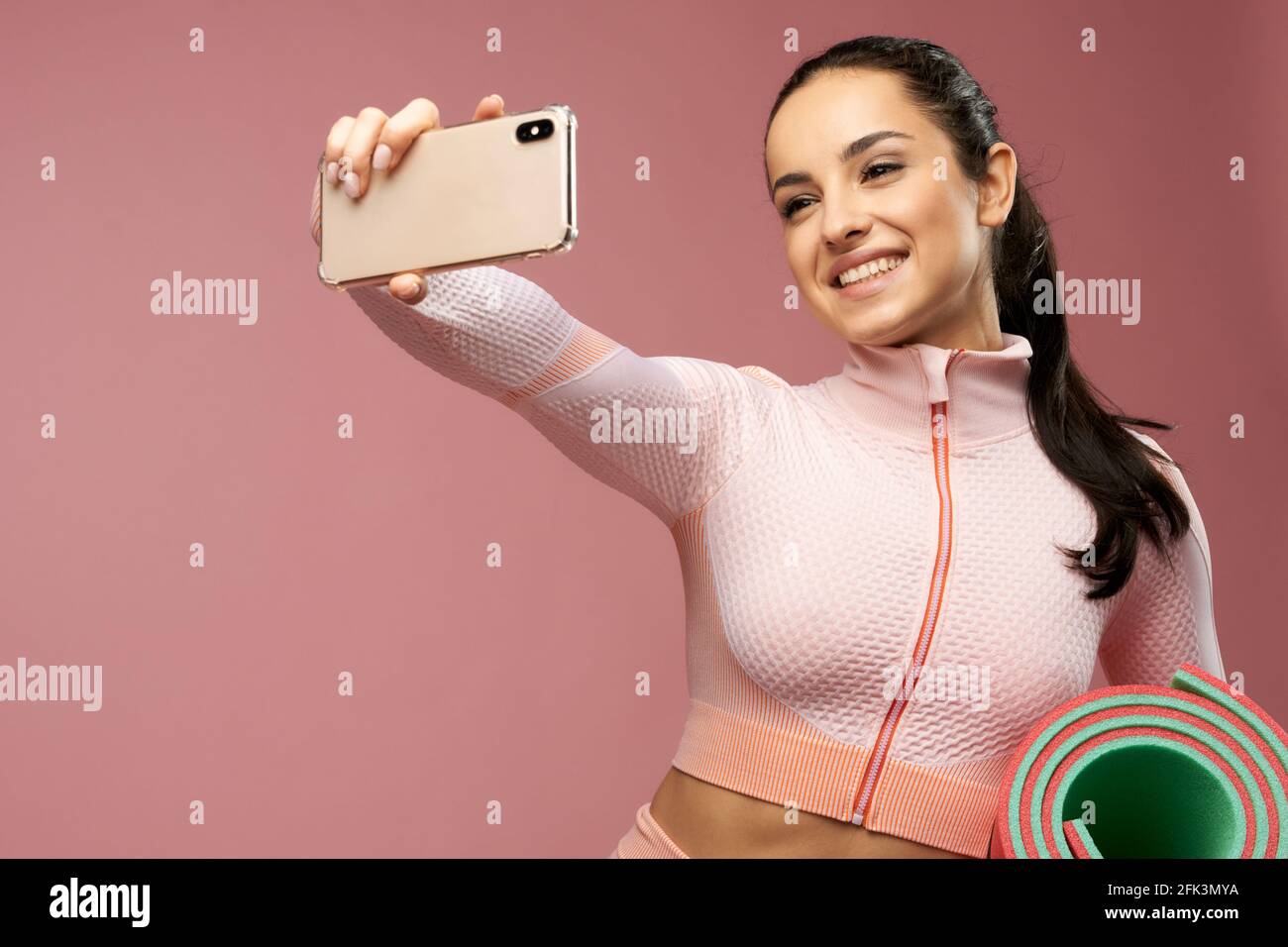 Cheerful young woman with yoga mat making selfie Stock Photo