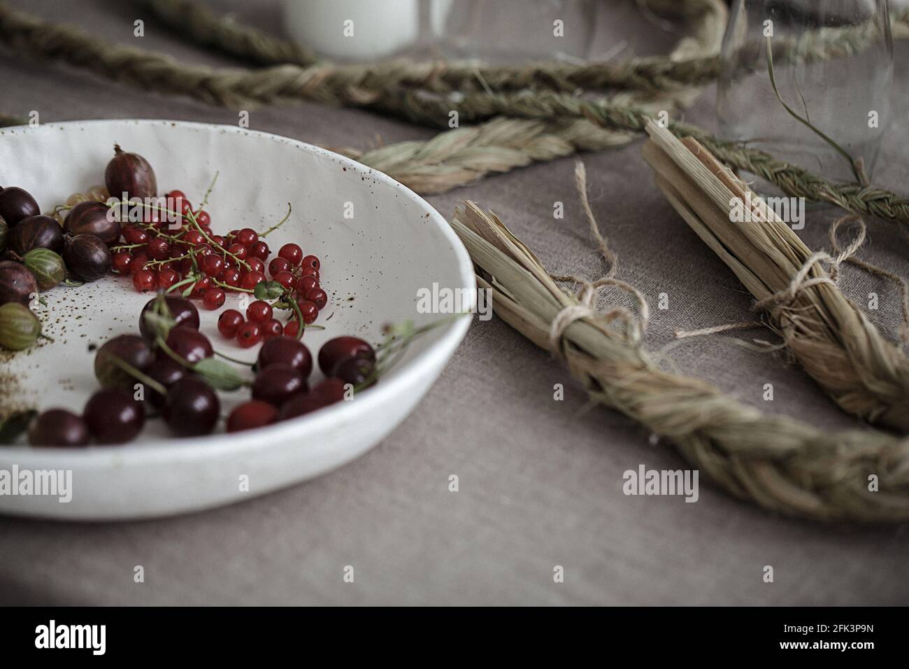 Craft white plate filled with gooseberries and red currants. Country rustic linen table set up Stock Photo