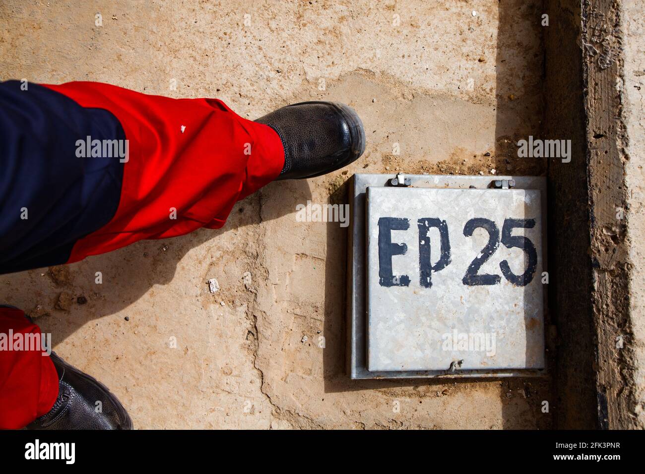 Oil refinery. Worker's legs and boots near manhole on concrete floor. Hand-man sign EP-25. Abstract industrial photo. Stock Photo