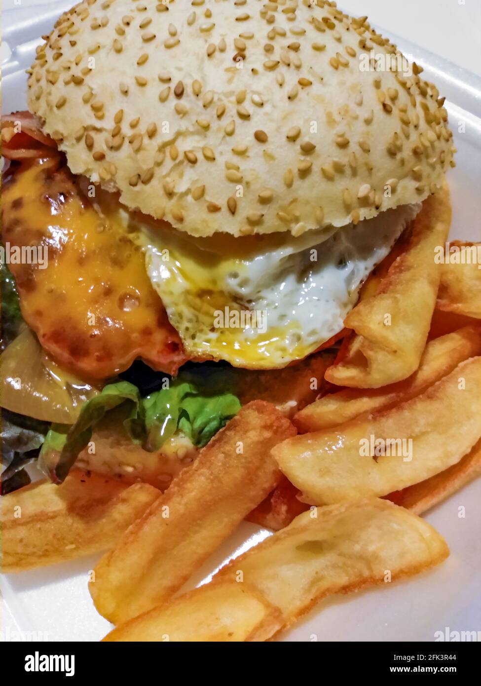 Burger with bacon, egg and melted cheese with french fries on the side
