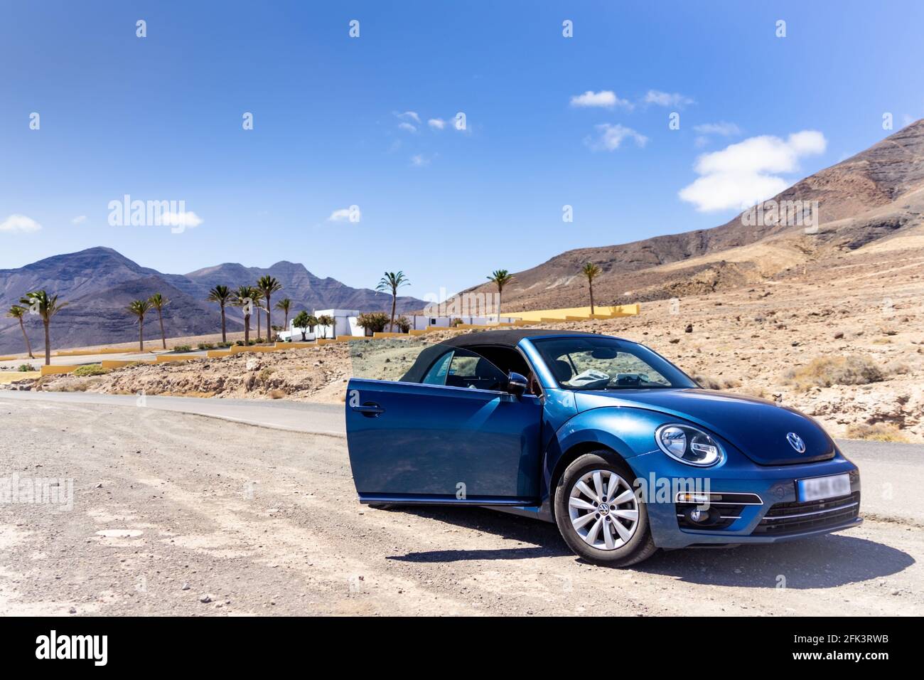 A metallic blue Beetle convertible standing before a lonely mansion in a desert landscape Stock Photo