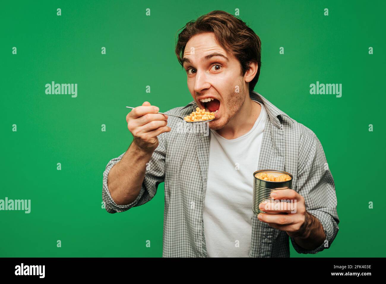 Young man eats corn in a jar, isolated on green background Stock Photo