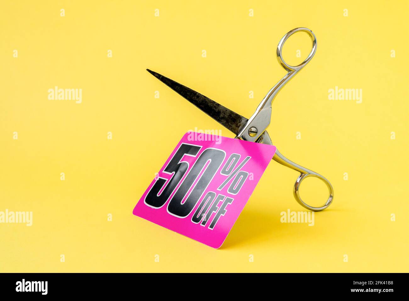 Metal scissors cutting the price tag on the yellow background. Cutting
