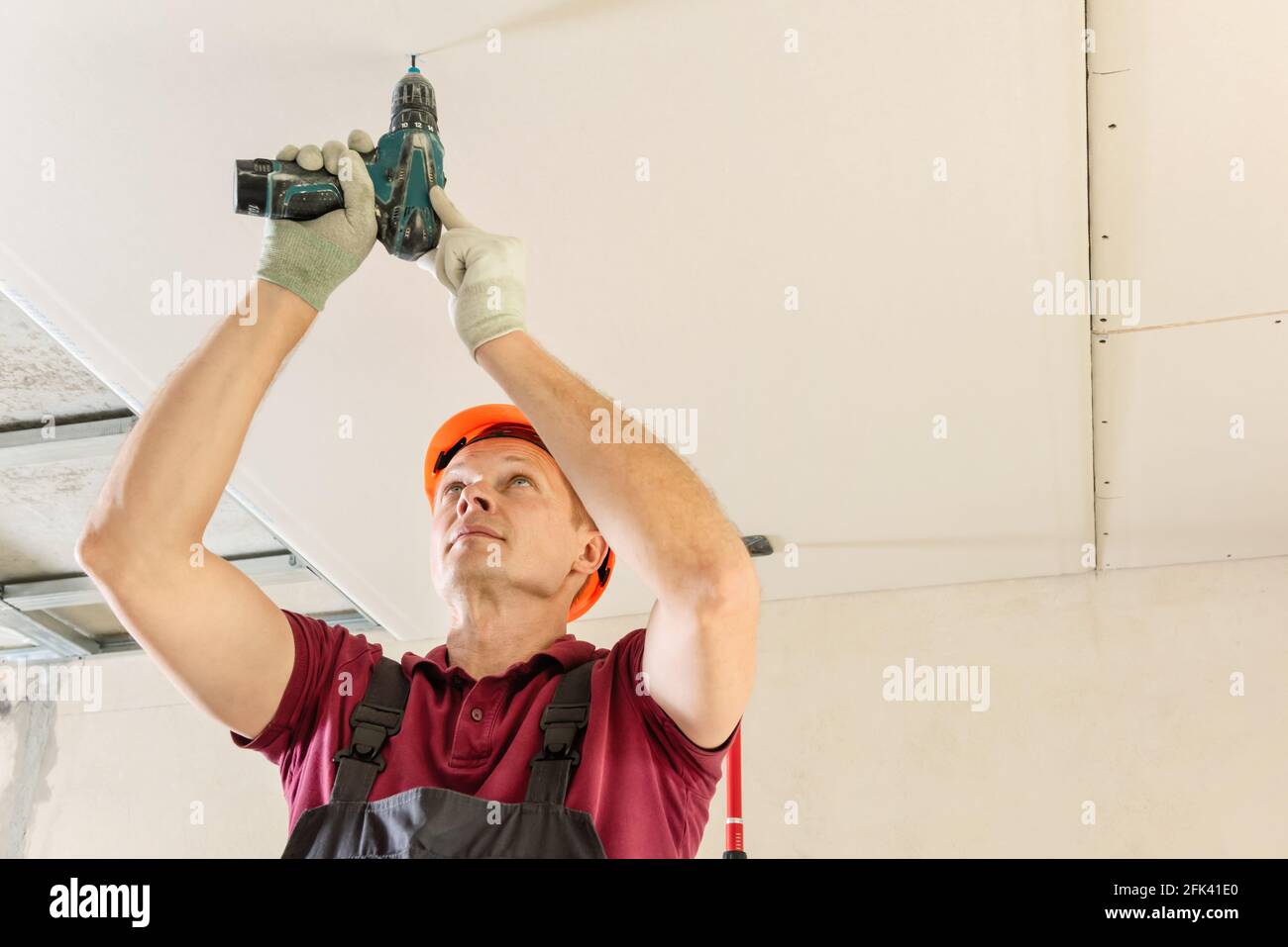 Installation of drywall. Worker is using screws and a screwdriver to