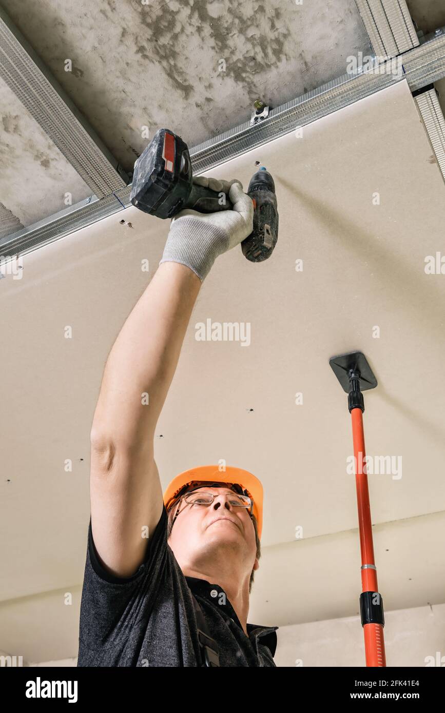 Installation of drywall. Worker is using screws and a screwdriver to
